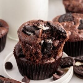 a close up shot of a Oreo Muffin stacked on top of another one with a bite taken out of it on a plate