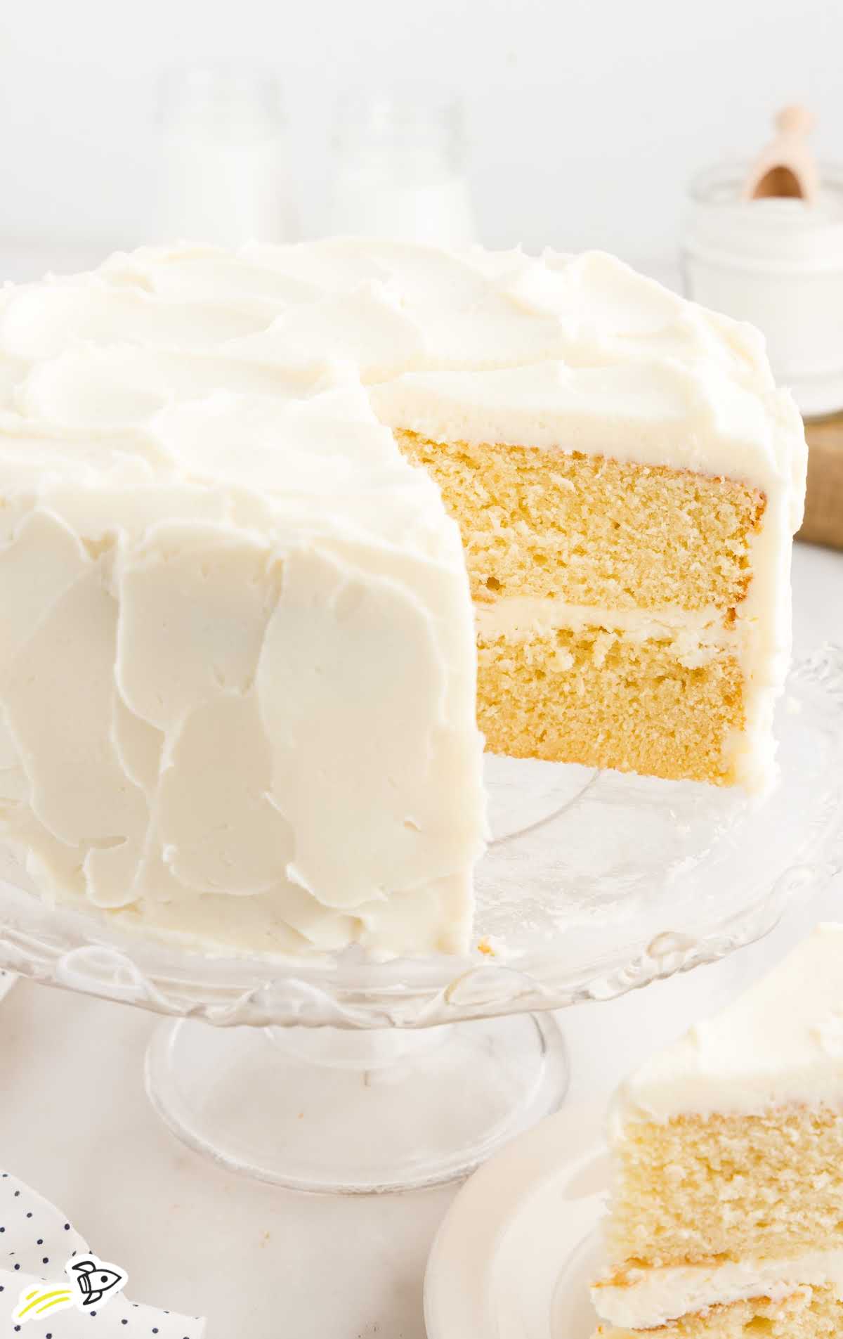 close up shot of a vanilla cake with a slice missing on a cake stand