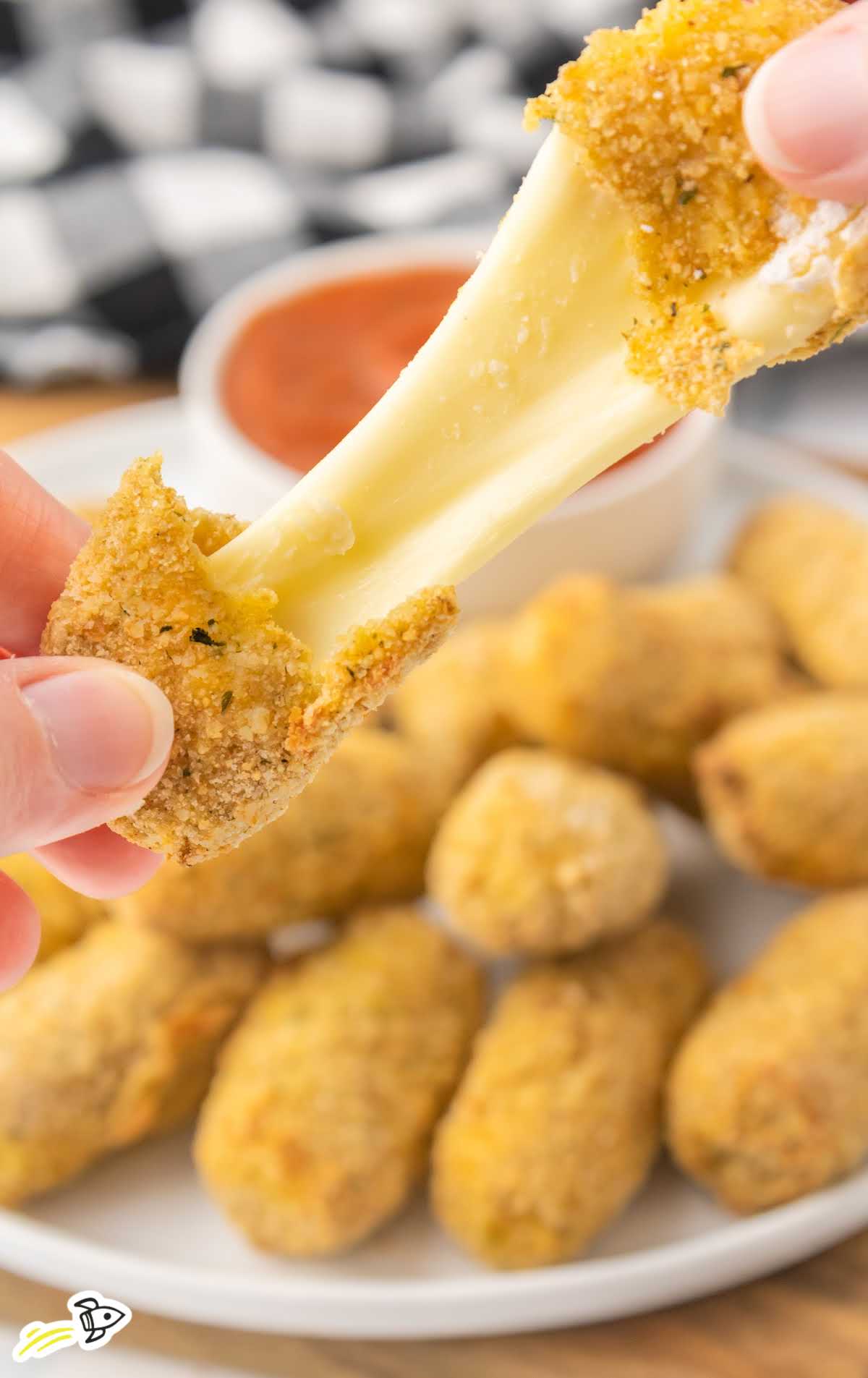 a close up shot of Air Fryer Mozzarella Sticks on a plate with one being pulled apart