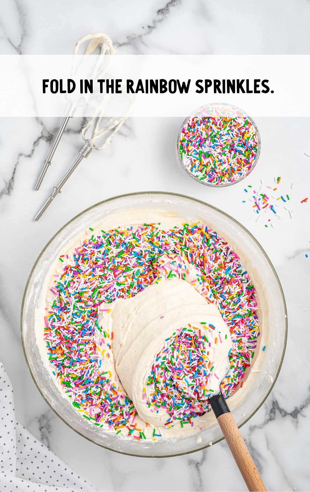rainbow sprinkles folded into the cake batter in a bowl