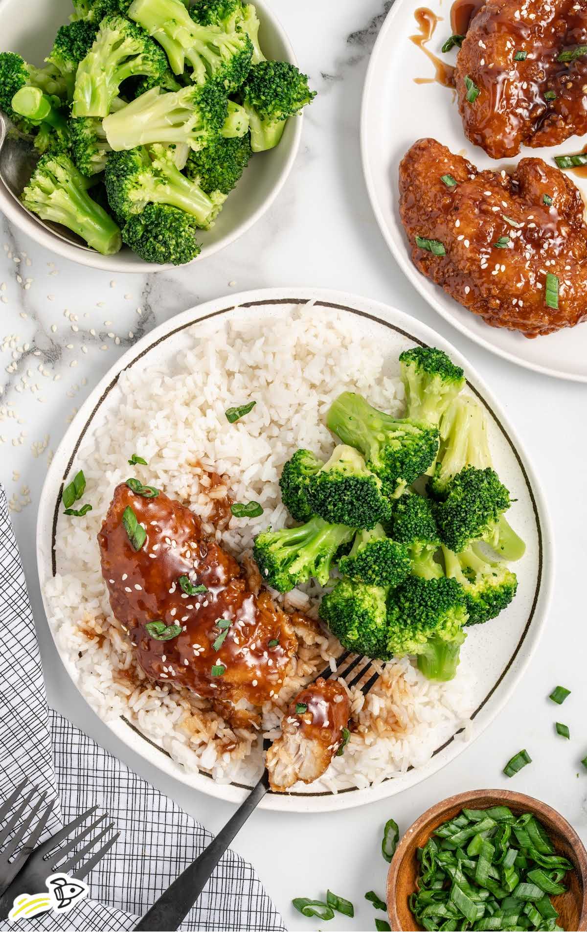 a plate Honey Garlic Chicken Breast topped with sesame seeds and green onions, broccoli, and white rice