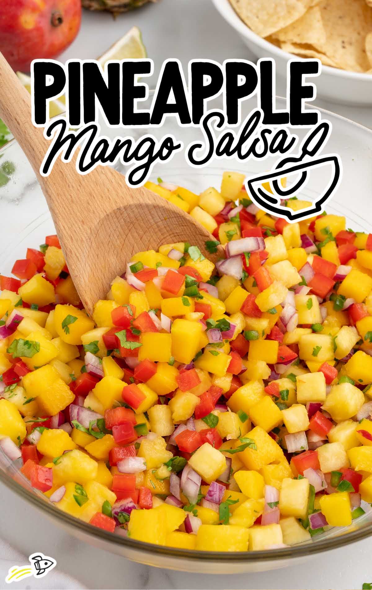 close up shot of Pineapple Mango Salsa in a bowl with a wooden spoon