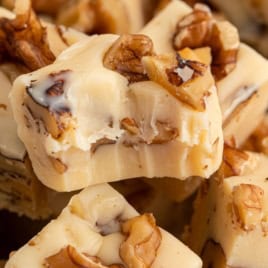 Close-up of creamy, light-colored Maple Walnut Fudge pieces with visible walnut chunks on top and inside, showing a smooth, rich texture and a freshly bitten edge on the central piece.