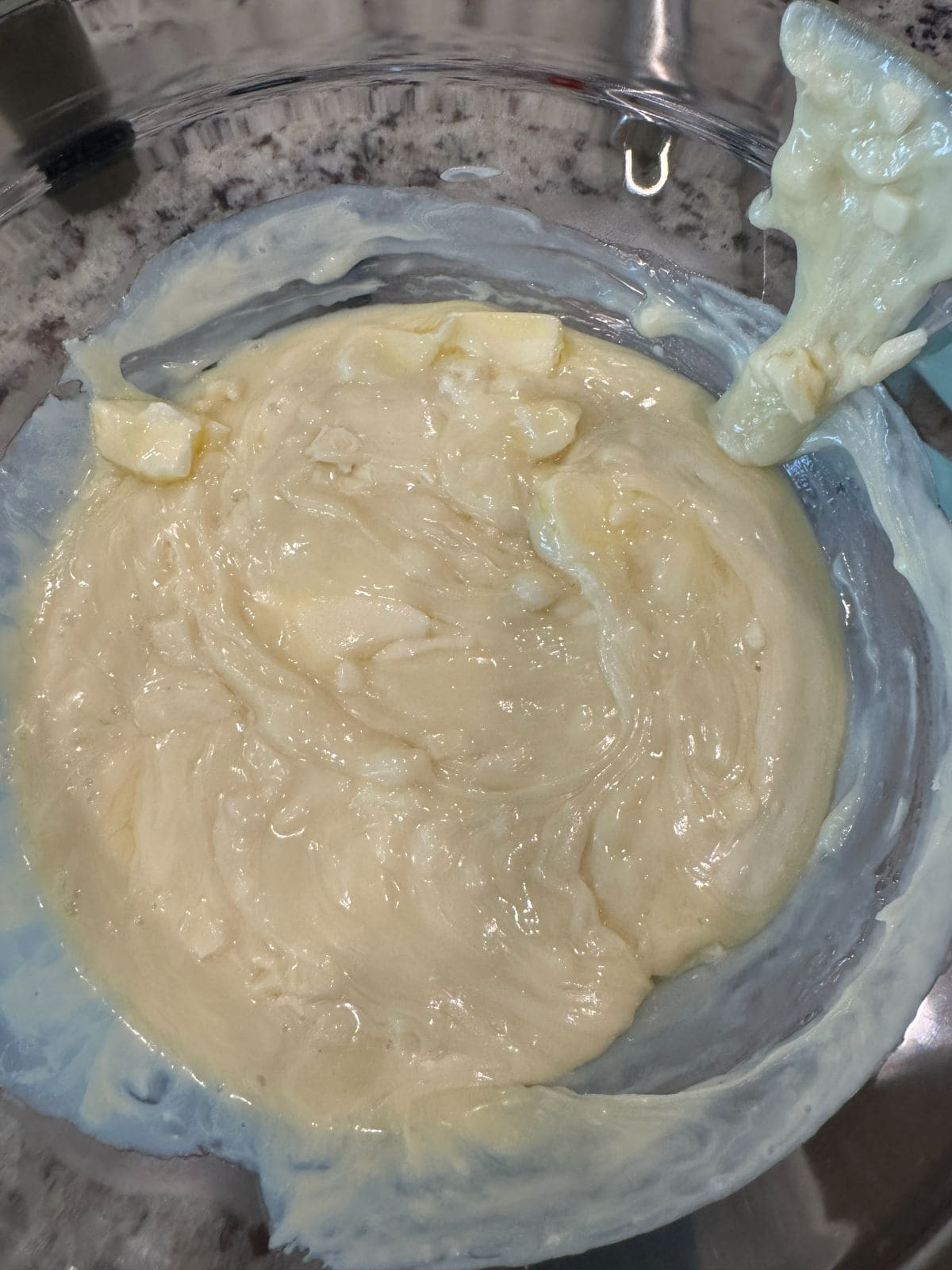 A clear glass bowl filled with thick, creamy, light yellow Maple Walnut Fudge batter, with some of the luscious mixture clinging to the edge and rim of the bowl.