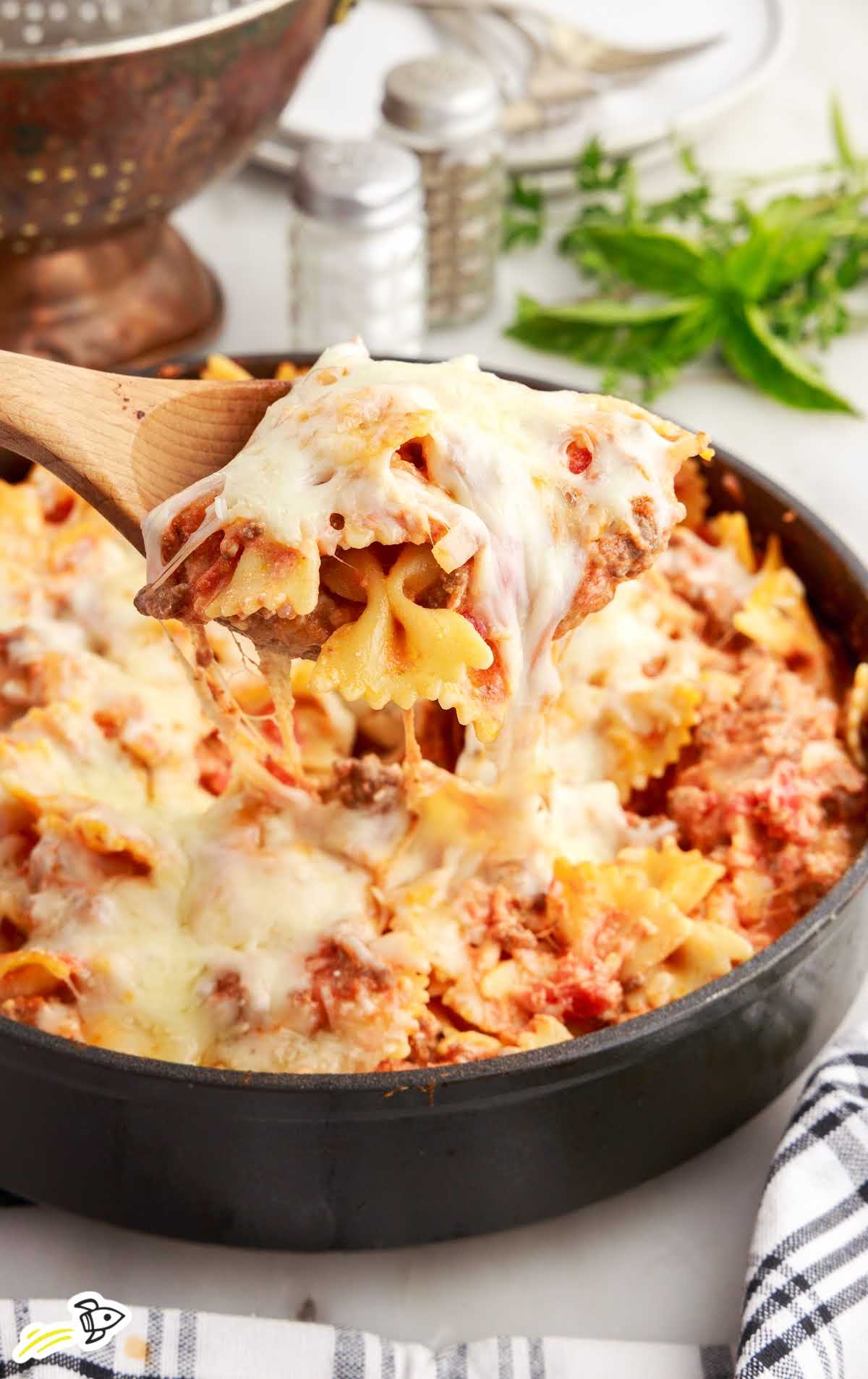 close up shot of Bow Tie Lasagna in a skillet with a spoon grabbing a piece
