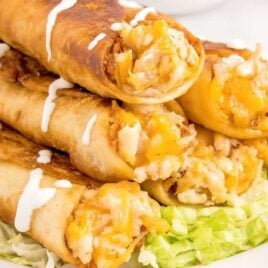 close up shot of a plate of Chicken Flautas topped on a bead of avocado