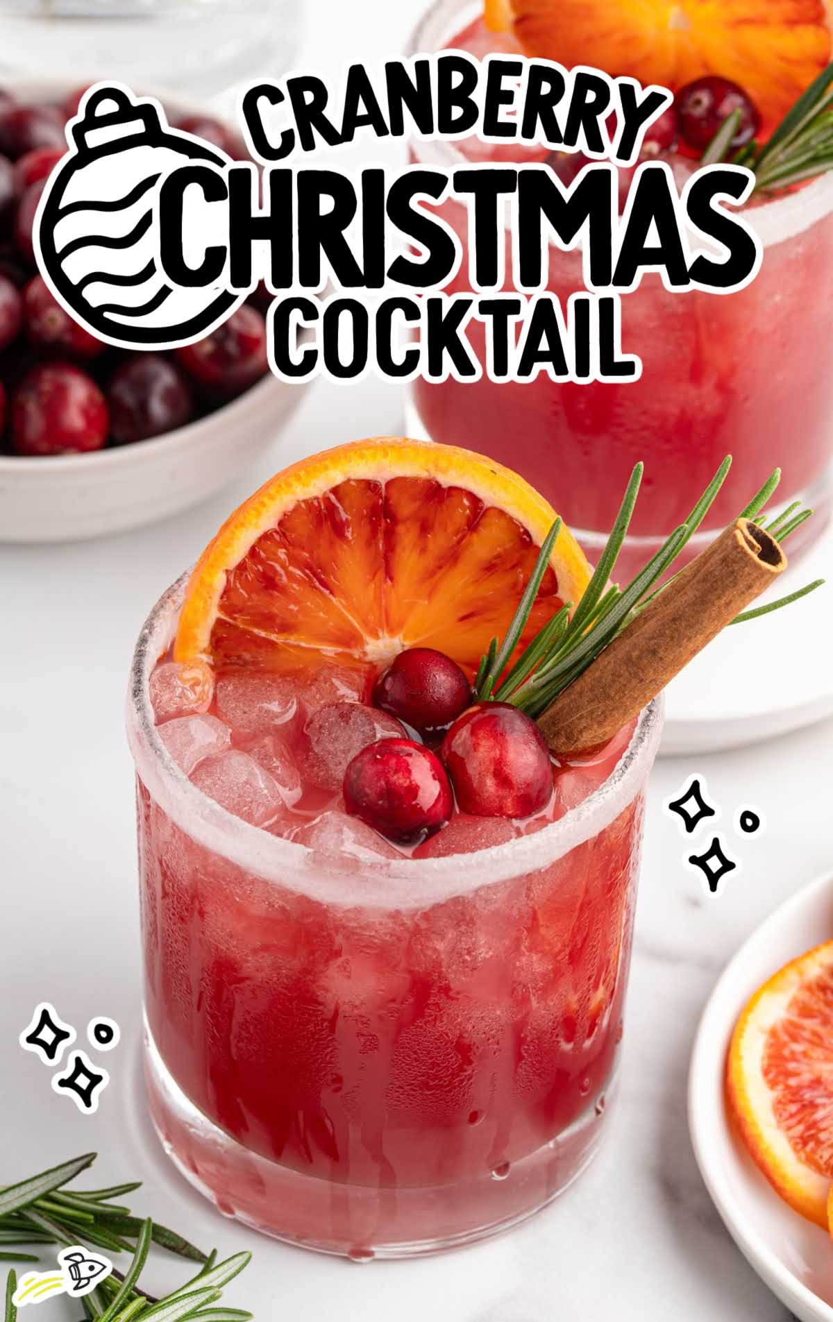 Cranberry Christmas cocktail served in a glass with ice, orange slice, cranberries, rosemary, and a cinnamon stick.