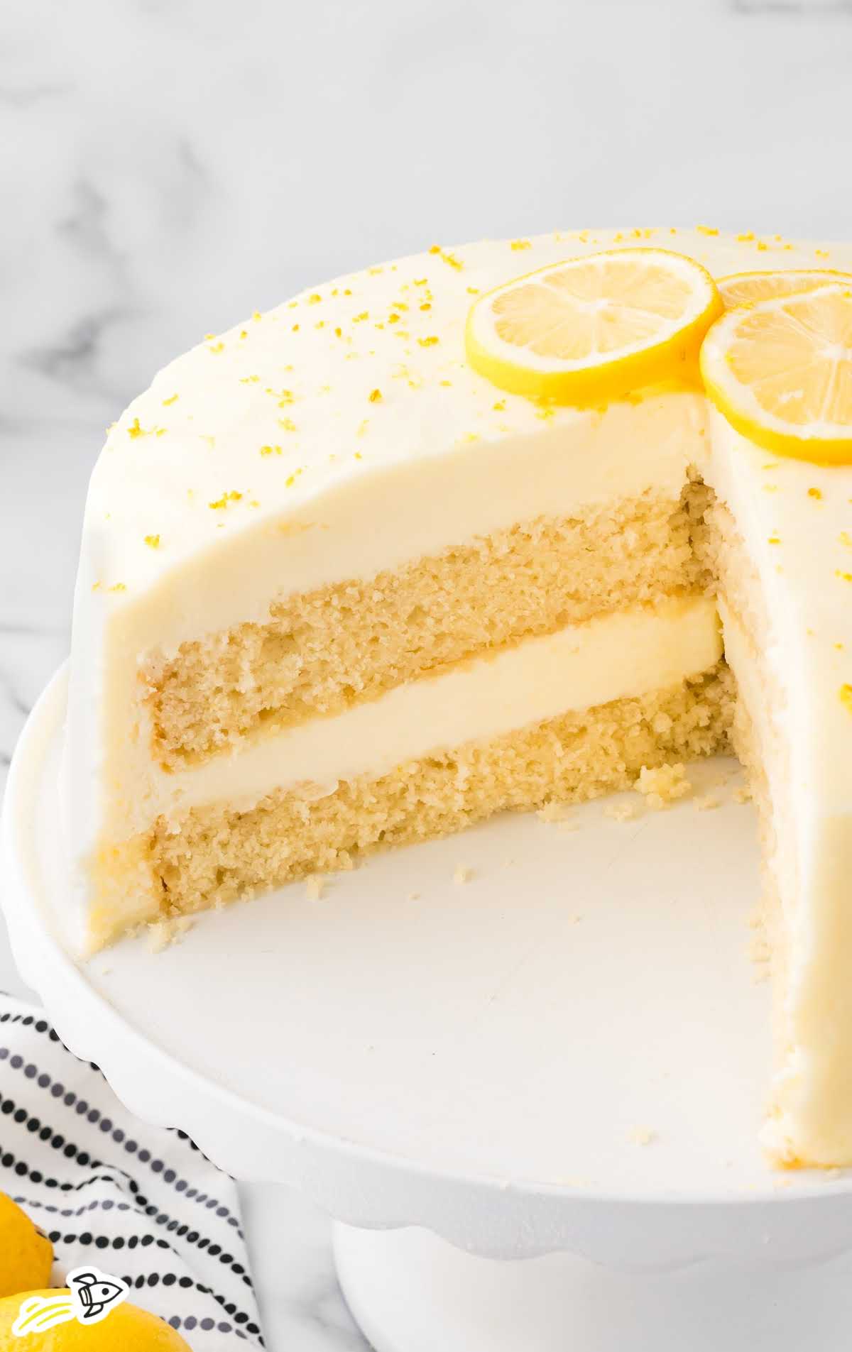 Lemon Velvet Cake on a cake stand topped with slices of lemon and a slice of cake missing