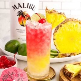 a close up shot of Malibu Cocktail garnished with a cherry, sliced pineapple, and a slice of lime