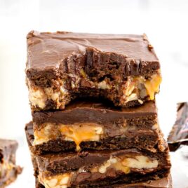 a close up shot of Snickers Brownies stacked on top of each other with one having a bite taken out of it