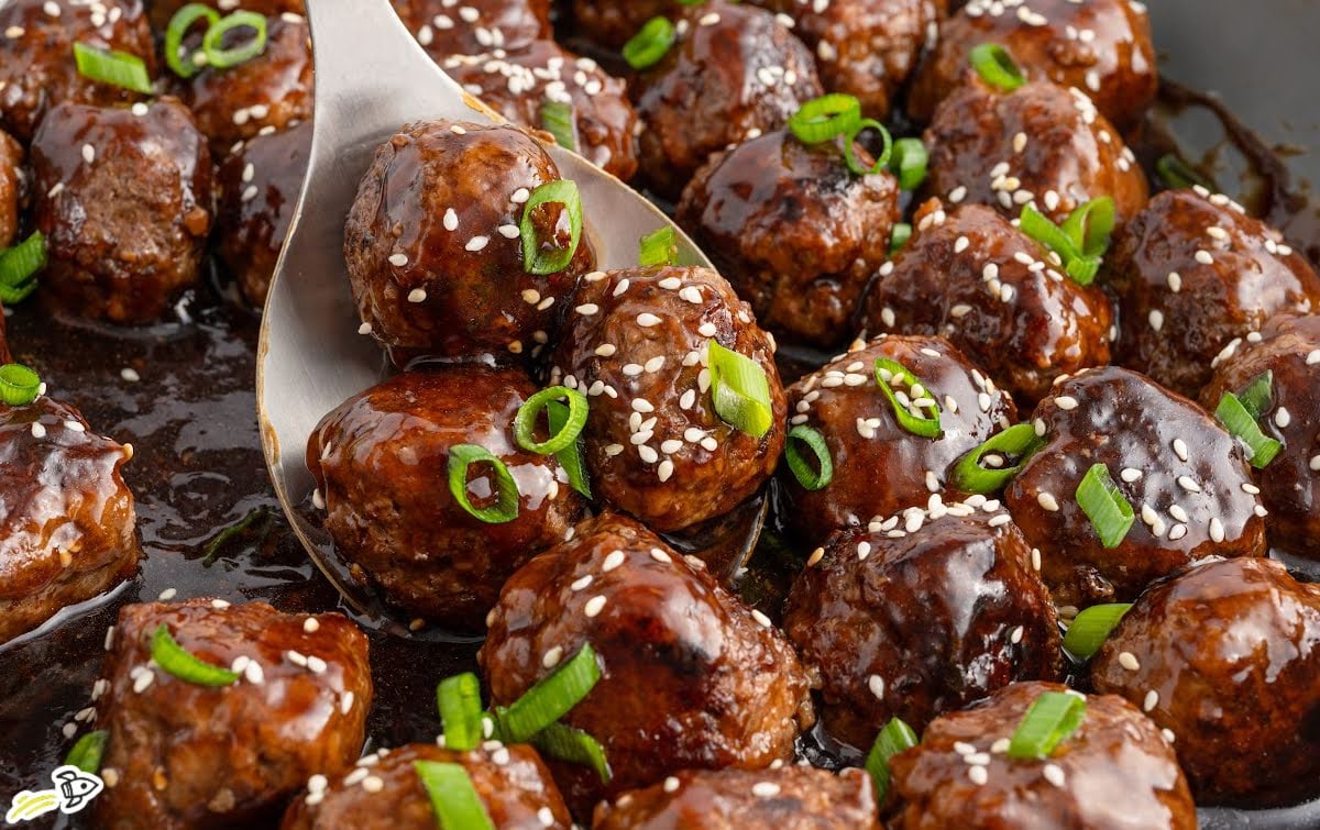 Glazed teriyaki meatballs topped with sesame seeds and green onions in a skillet