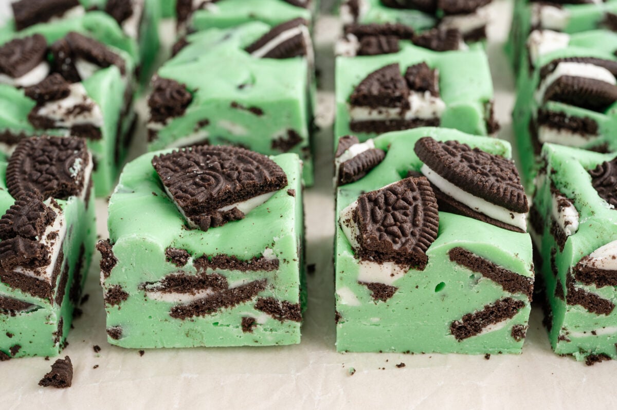 Rows of neatly sliced mint Oreo fudge squares arranged on parchment paper. Each piece is packed with visible cookie layers and topped with Oreo chunks.