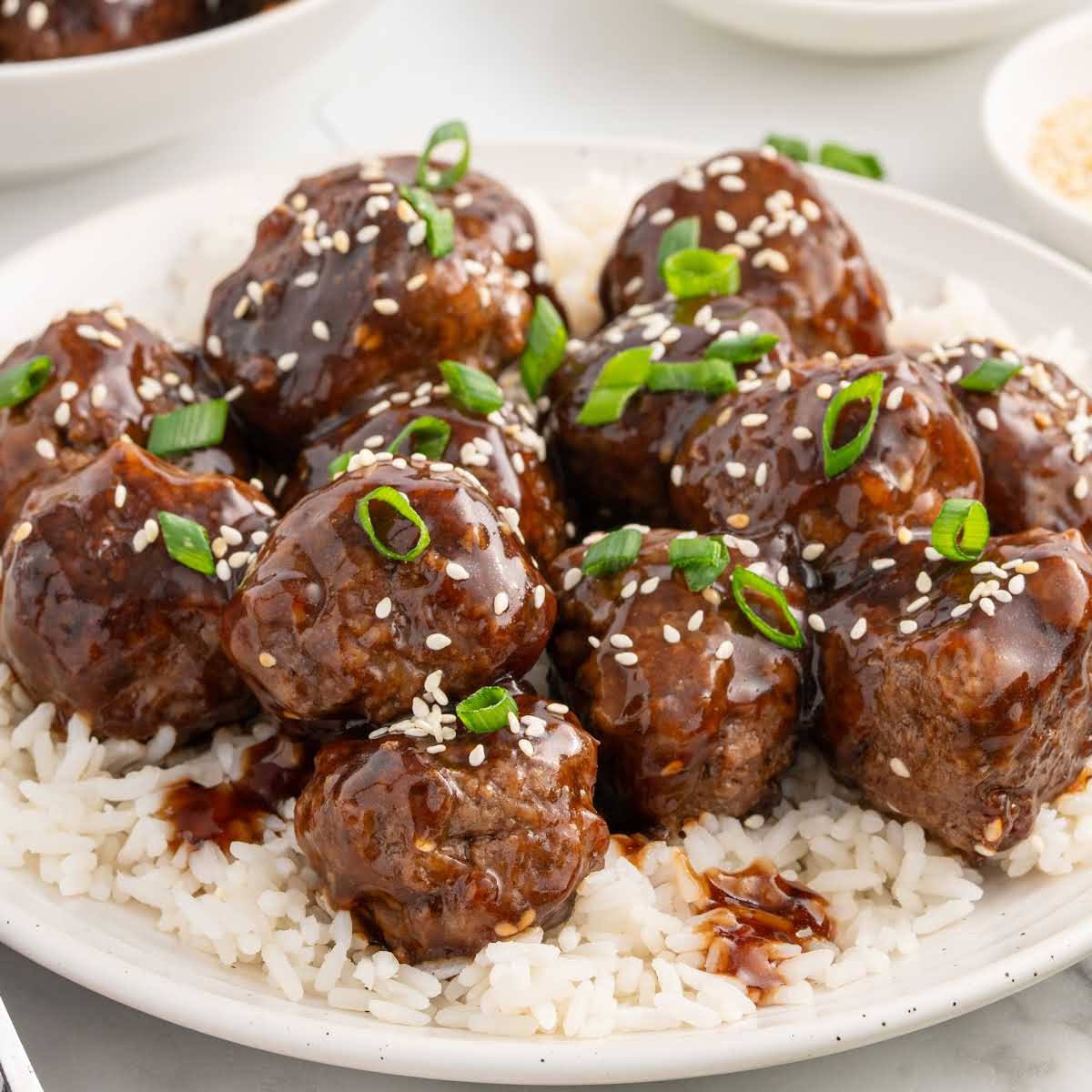 Plate of teriyaki meatballs served over steamed white rice with sesame seeds and green onions