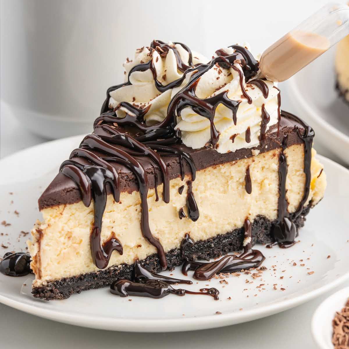 Baileys cheesecake slice with smooth chocolate ganache, whipped cream, and chocolate drizzle served on a white plate.
