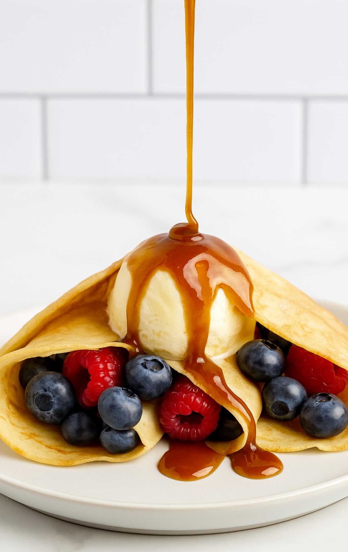 Brown sugar sauce drizzled over vanilla ice cream inside folded crepes with fresh blueberries and raspberries