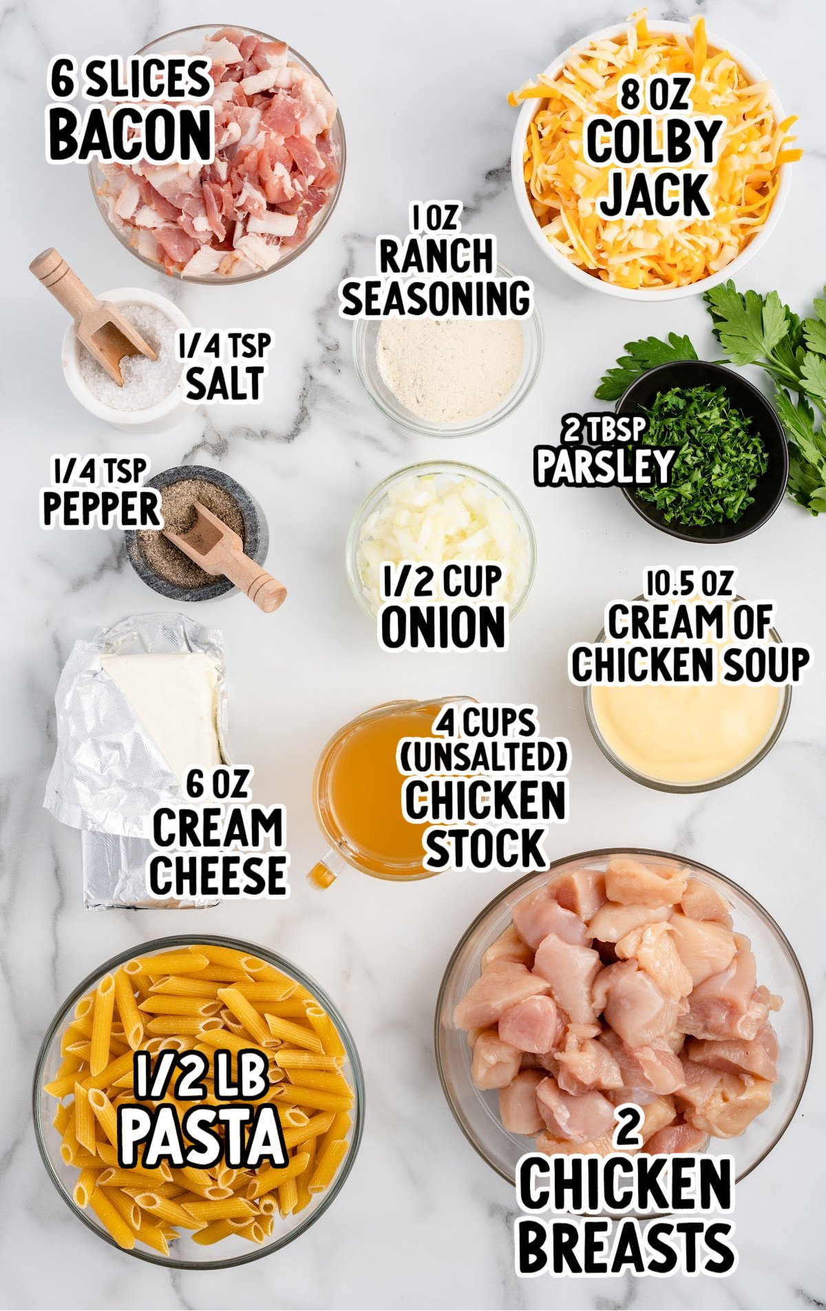 Overhead view of labeled ingredients for Crack Chicken Penne on a white marble surface. Items include: 6 slices chopped bacon, 8 oz shredded Colby Jack cheese, 1 oz ranch seasoning, 2 tablespoons chopped parsley, ½ cup chopped onion, 10.5 oz cream of chicken soup, 2 raw diced chicken breasts, 4 cups unsalted chicken stock, 6 oz cream cheese, ½ lb penne pasta, ¼ teaspoon salt, and ¼ teaspoon pepper.