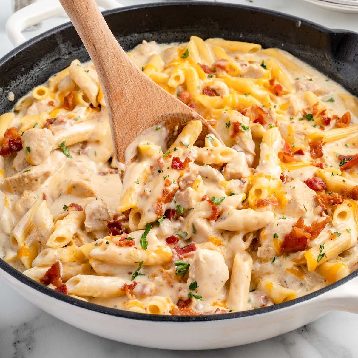 chicken penne garnished with parsley and bacon bits in a skillet