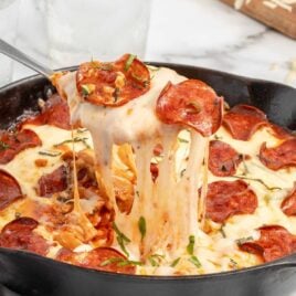 a skillet of pizza garnished with basil with a spoon