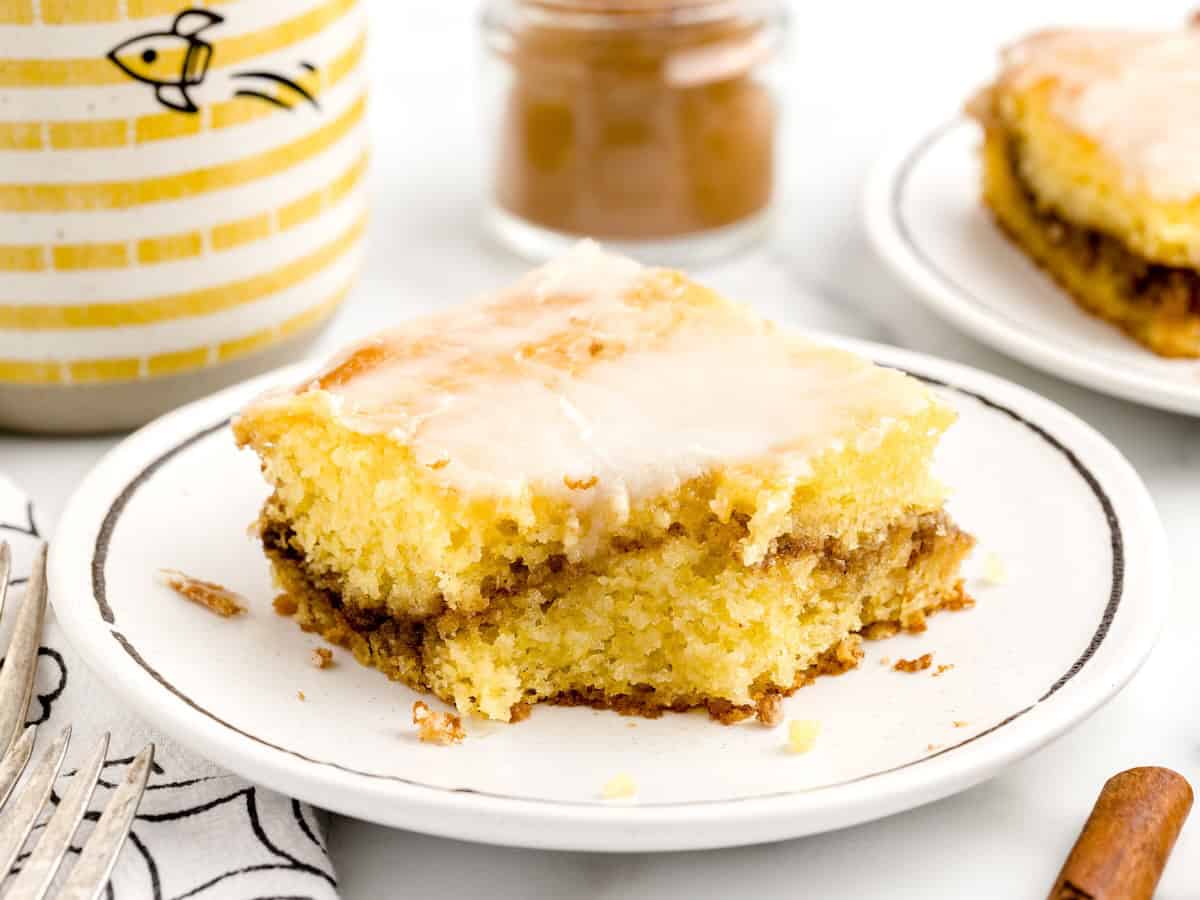 A square of honey bun cake with a cinnamon swirl and white glaze on a small plate.