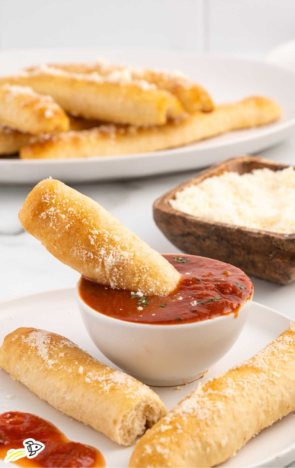 a breadstick dipped into a bowl of marinara sauce