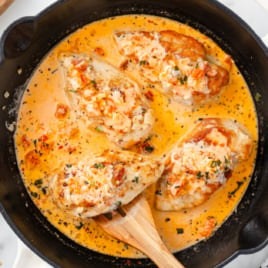 a skillet of marry me chicken with a spatula lifting out a piece.