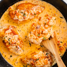 a cast iron skillet of marry me chicken with a spatula lifting out a piece.