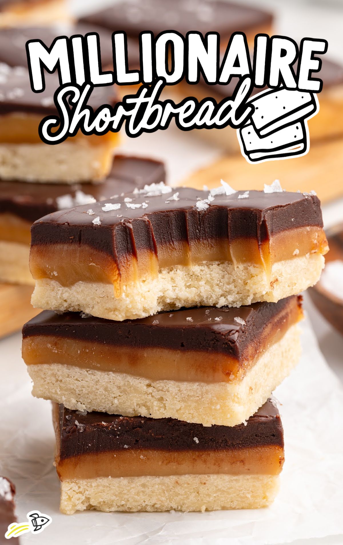 Stack of millionaire shortbread squares with bite taken to show thick caramel and chocolate layers over buttery shortbread base
