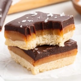 Two millionaire shortbread squares stacked on parchment paper with visible shortbread crust, golden caramel, and chocolate topping
