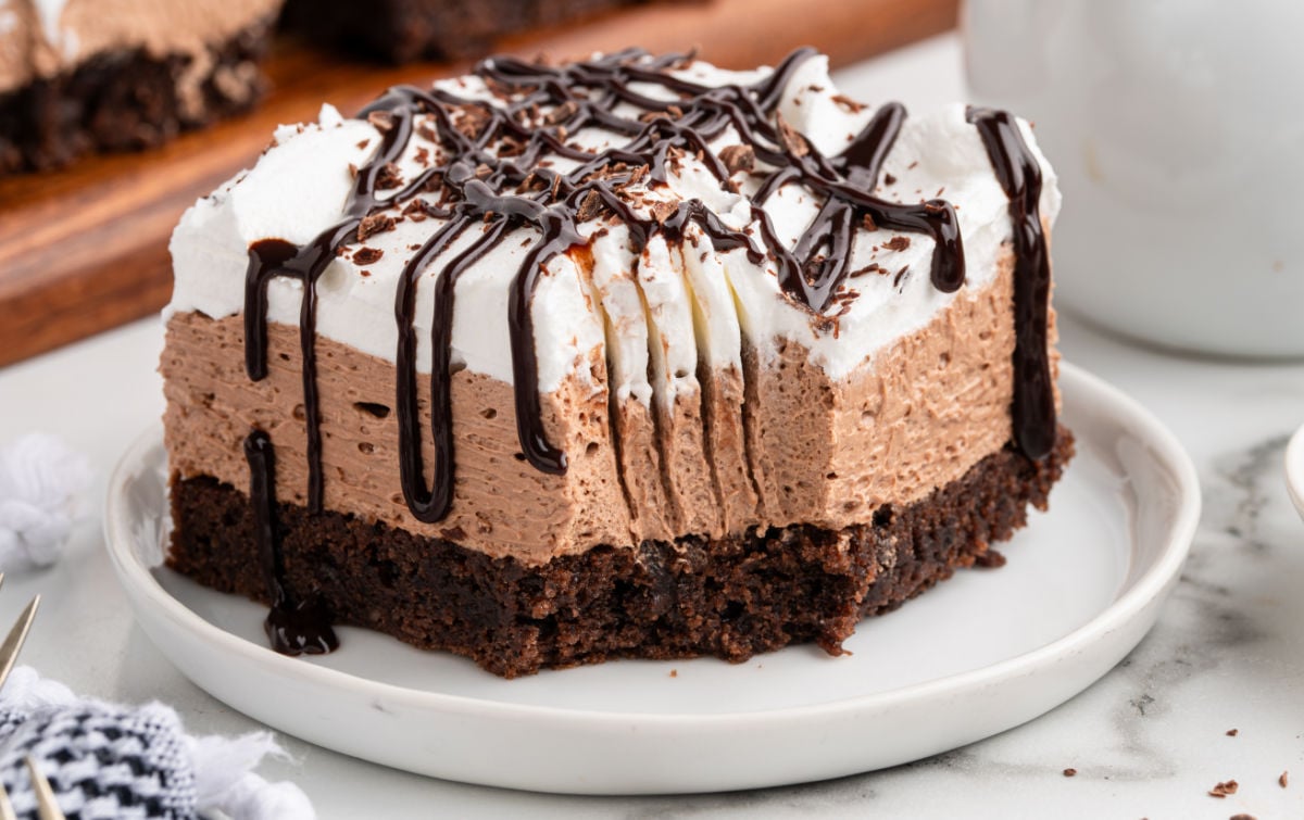 A close-up view of one French silk brownie slice on a plate, topped with whipped cream, chocolate drizzle, and chocolate shavings. The rich, mousse-like layer and fudgy brownie base are clearly visible.