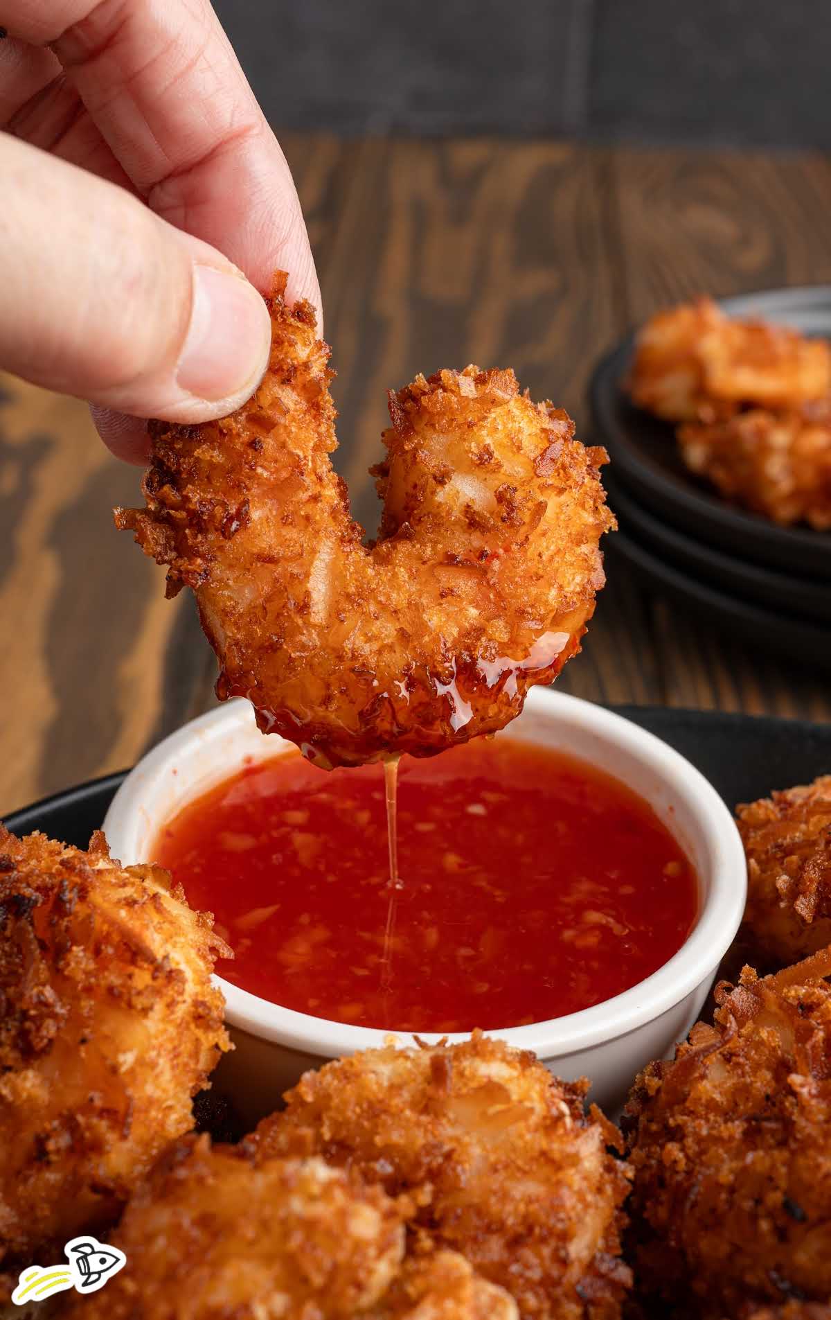 Hand dipping crispy coconut shrimp into sweet chili sauce with sauce dripping