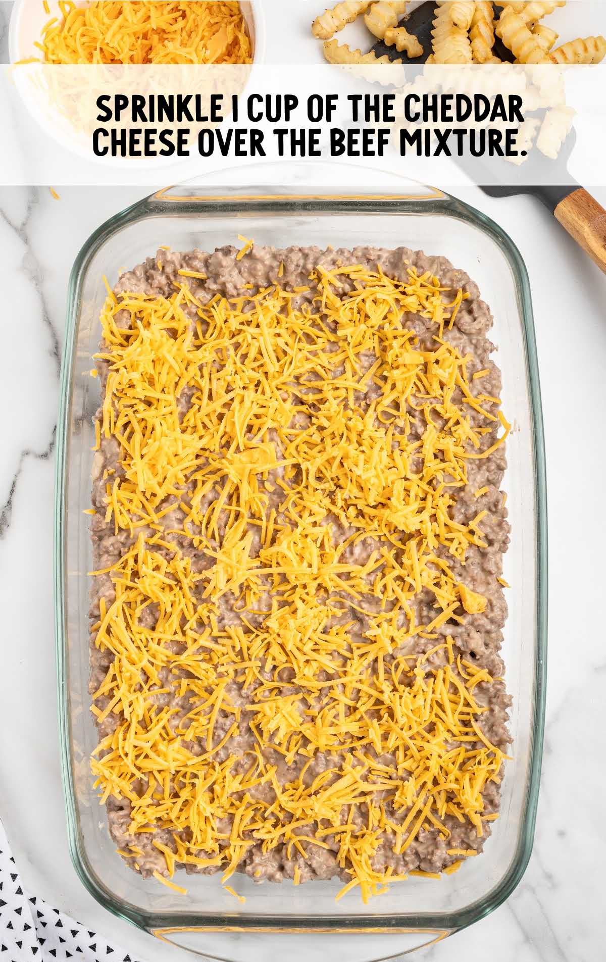 cheddar cheese sprinkled over the beef mixture in a baking dish