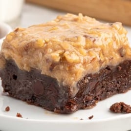 Thick German chocolate brownie square on a white plate with gooey coconut pecan topping.