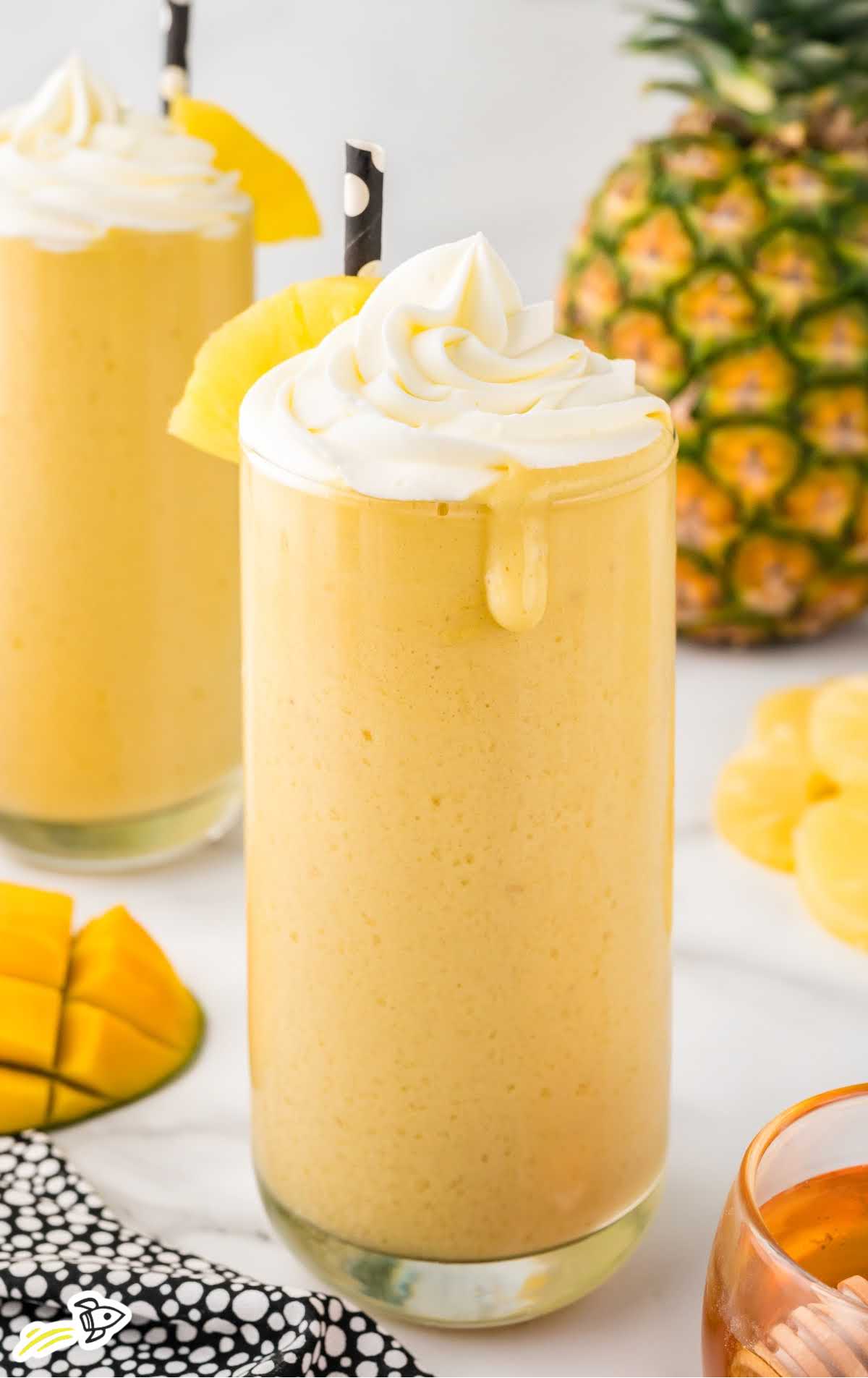 a close up shot of Mango Pineapple Smoothie in a tall glass topped with whipped cream