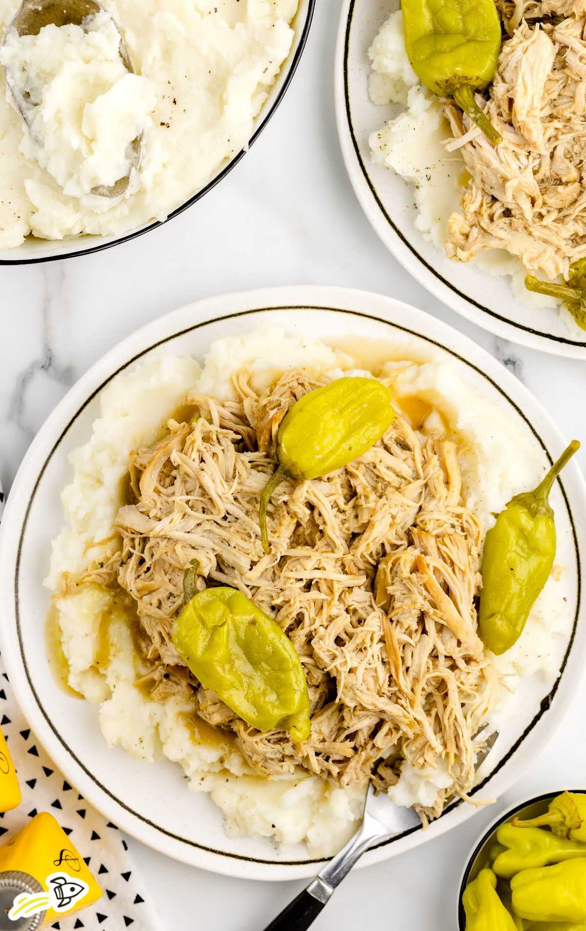 a plate of shredded chicken with pepperoncini served over a plate of mashed potatoes