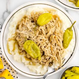 a plate of shredded chicken with pepperoncini served over a plate of mashed potatoes