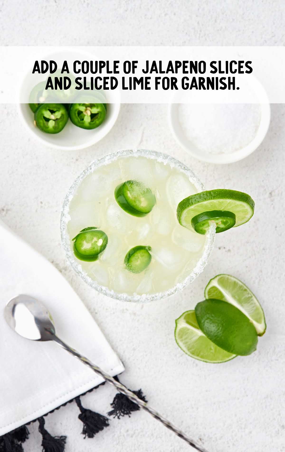a glass of Spicy Margarita garnished with slices of lime and jalapeños