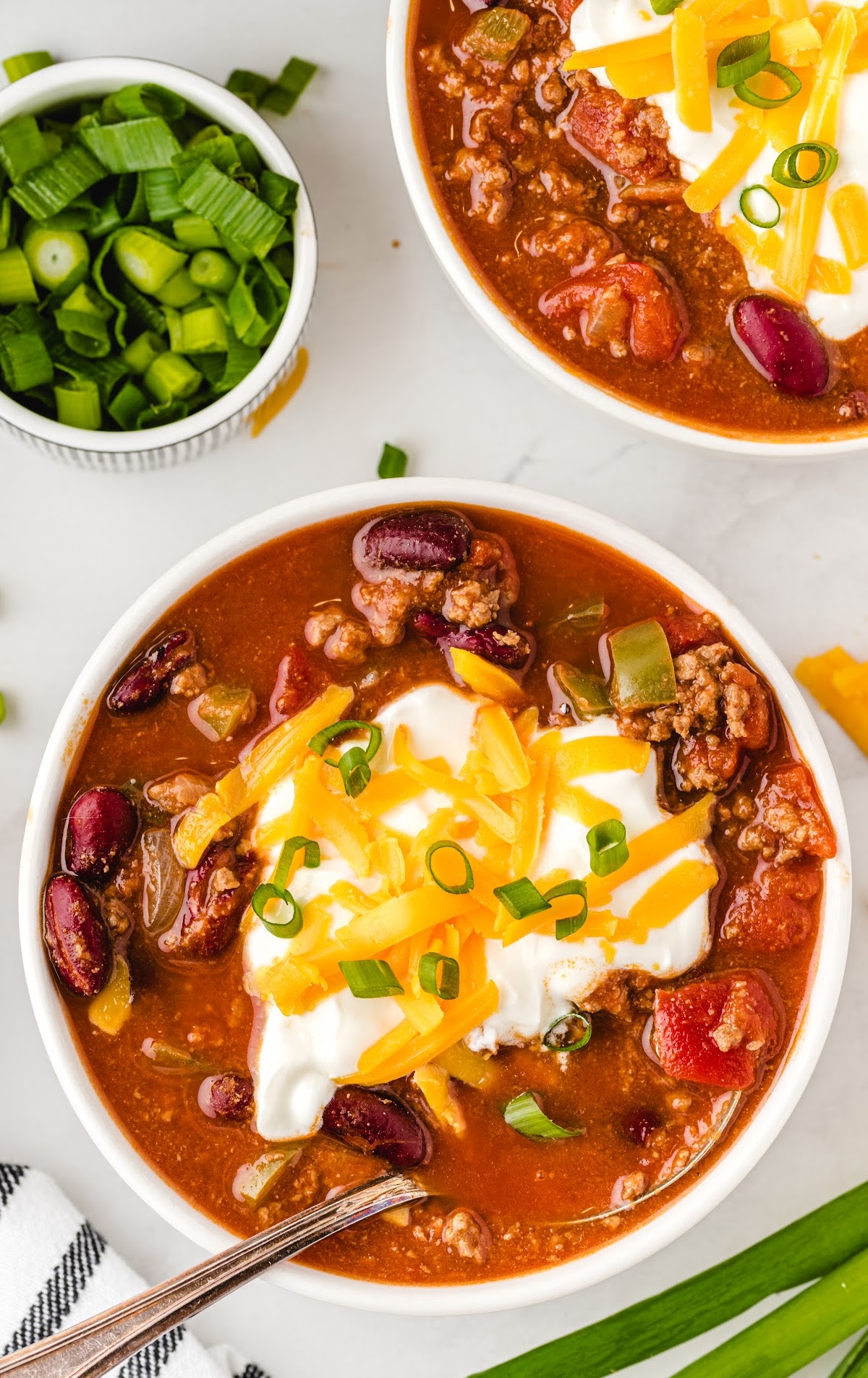 a bowl of chili topped with sour cream, shredded cheese, and green onion with a spoon