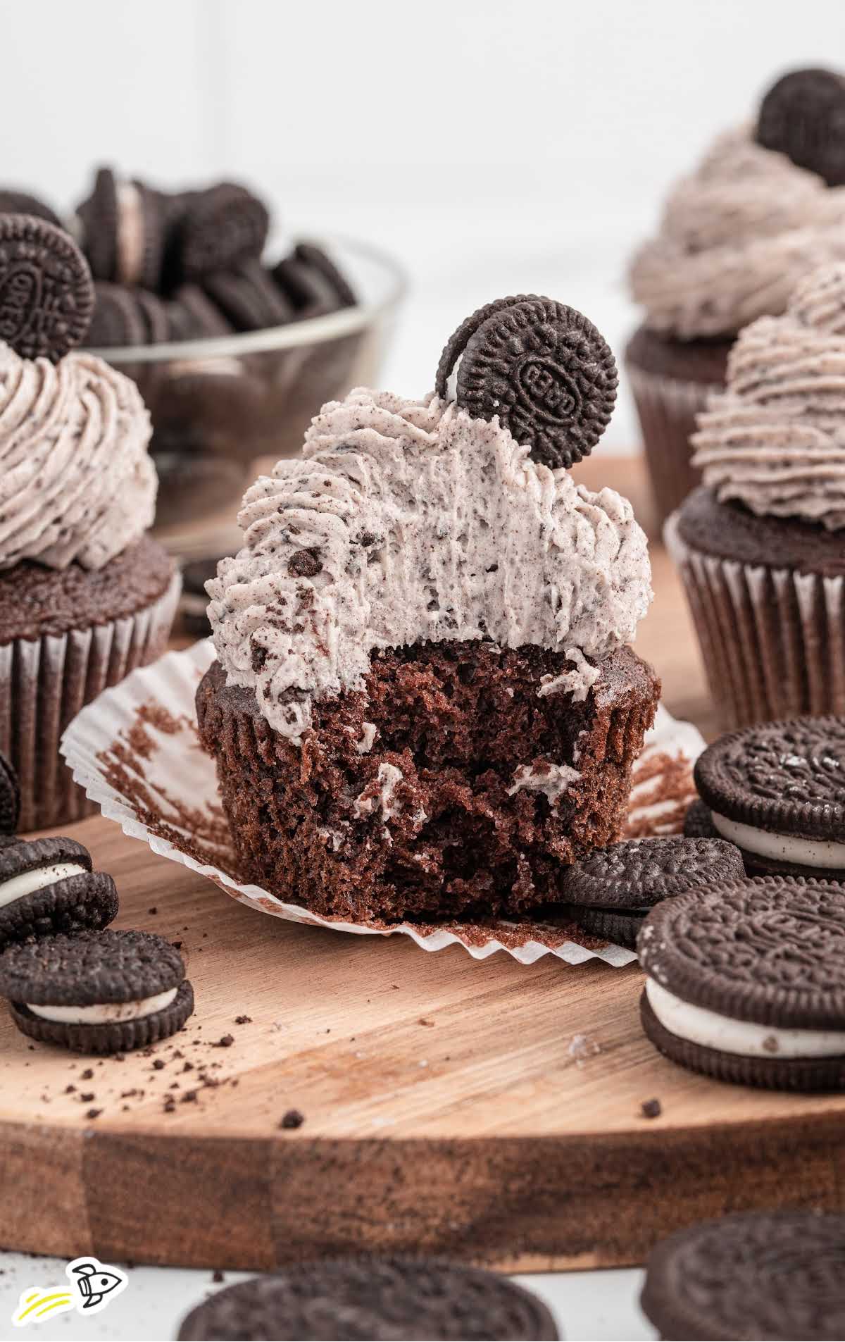a frosted cupcake topped with a Oreo with a bite taken out of the cupcake