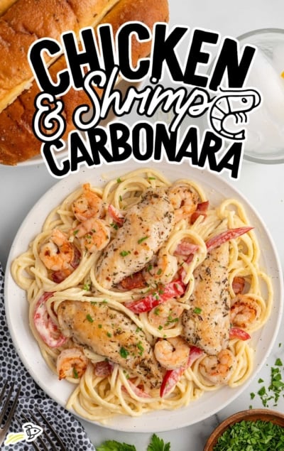 Chicken and shrimp carbonara on a white plate with creamy pasta, shrimp, bell peppers, and herbs.