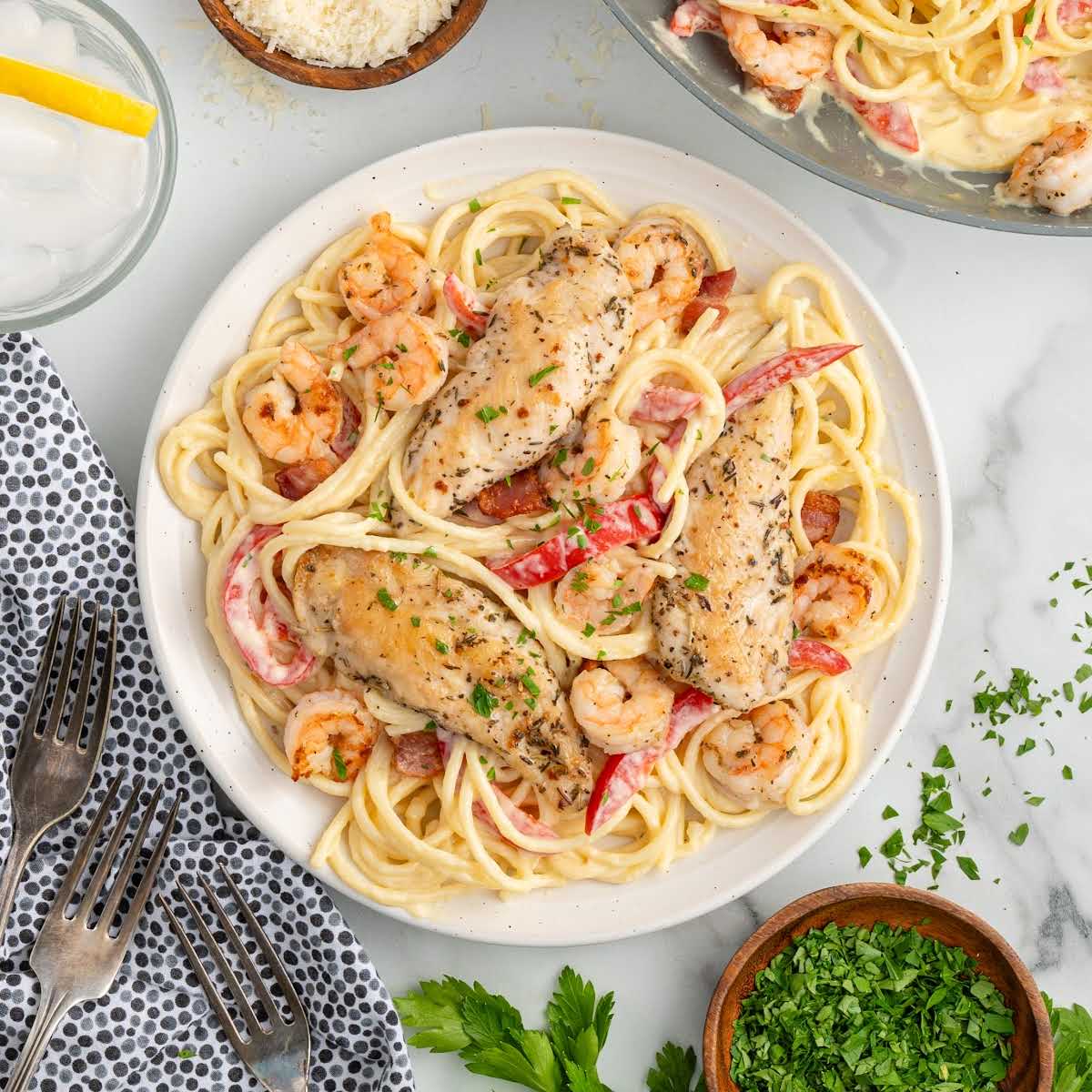 Overhead view of a plated chicken and shrimp carbonara meal with garnishes and table setting.
