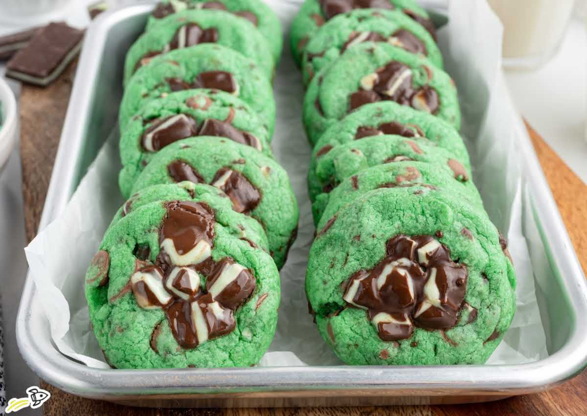 Mint chocolate chip cookies arranged in rows in a parchment lined baking pan with melted chocolate centers visible