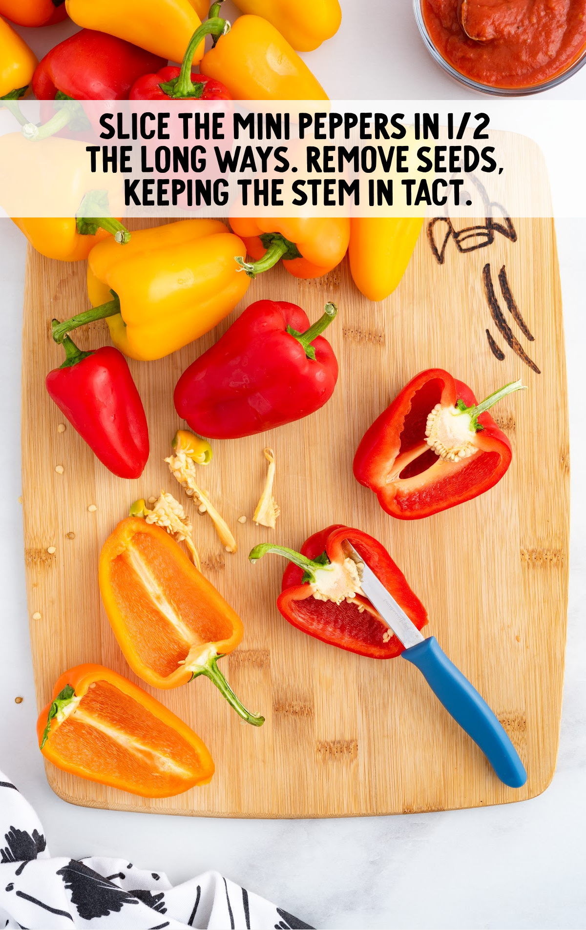 A cutting board with mini peppers on it. They are being cut in half and cleaned of the seeds.