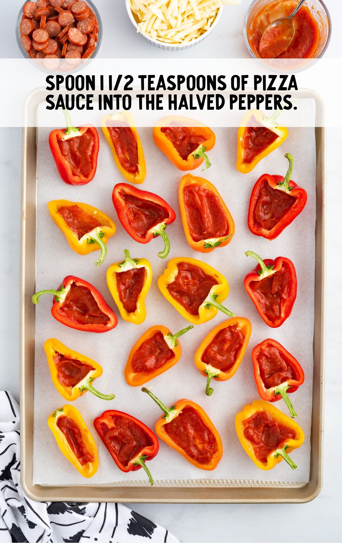 A baking tray is covered in mini peppers with sauce in them.