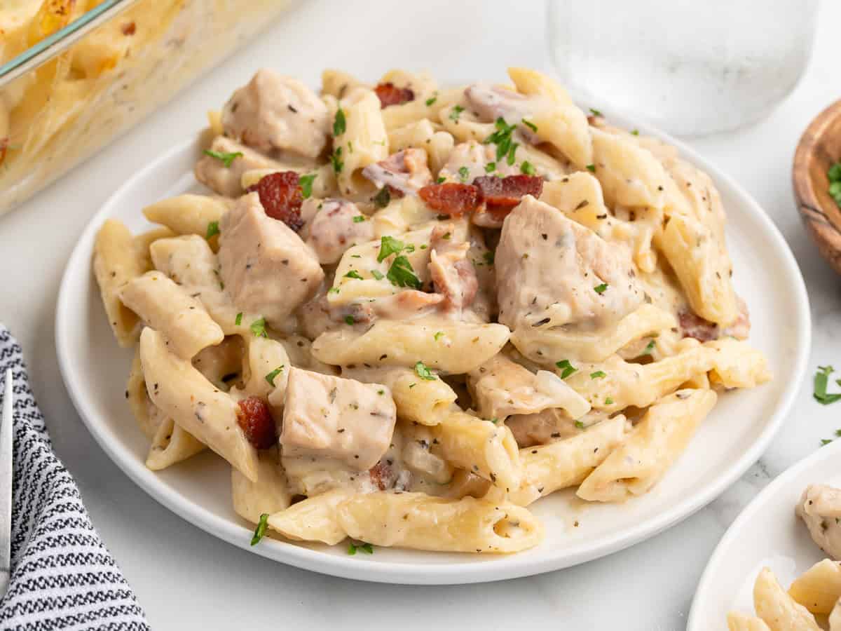 A plate of creamy penne pasta with chunks of chicken, pieces of bacon, and a sprinkling of chopped parsley on top, reminiscent of a delicious Chicken Bacon Ranch Casserole.