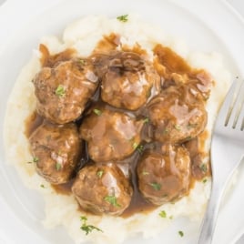 Meatballs and gravy on a white dinner plate with mashed potatoes.