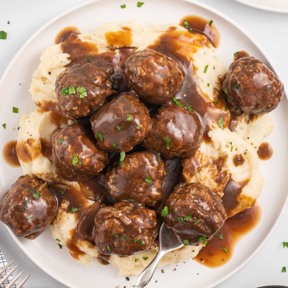 a plate of meatballs garnished with parsley and served over mashed potatoes