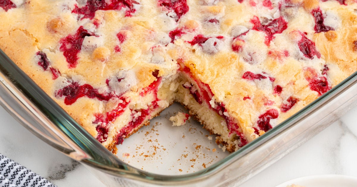 Baked cranberry cake in a glass dish with a section removed to show the tender inside and cranberry-studded top.