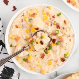 A bowl of thick and creamy-looking chicken corn chowder with a spoon it in, lifting out a bite.