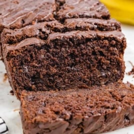 Sliced chocolate banana bread loaf with chocolate glaze, displayed on a marble cutting board.