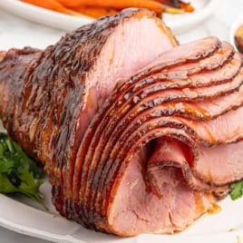 Whole spiral sliced ham with honey glaze served on a platter with fresh herbs.